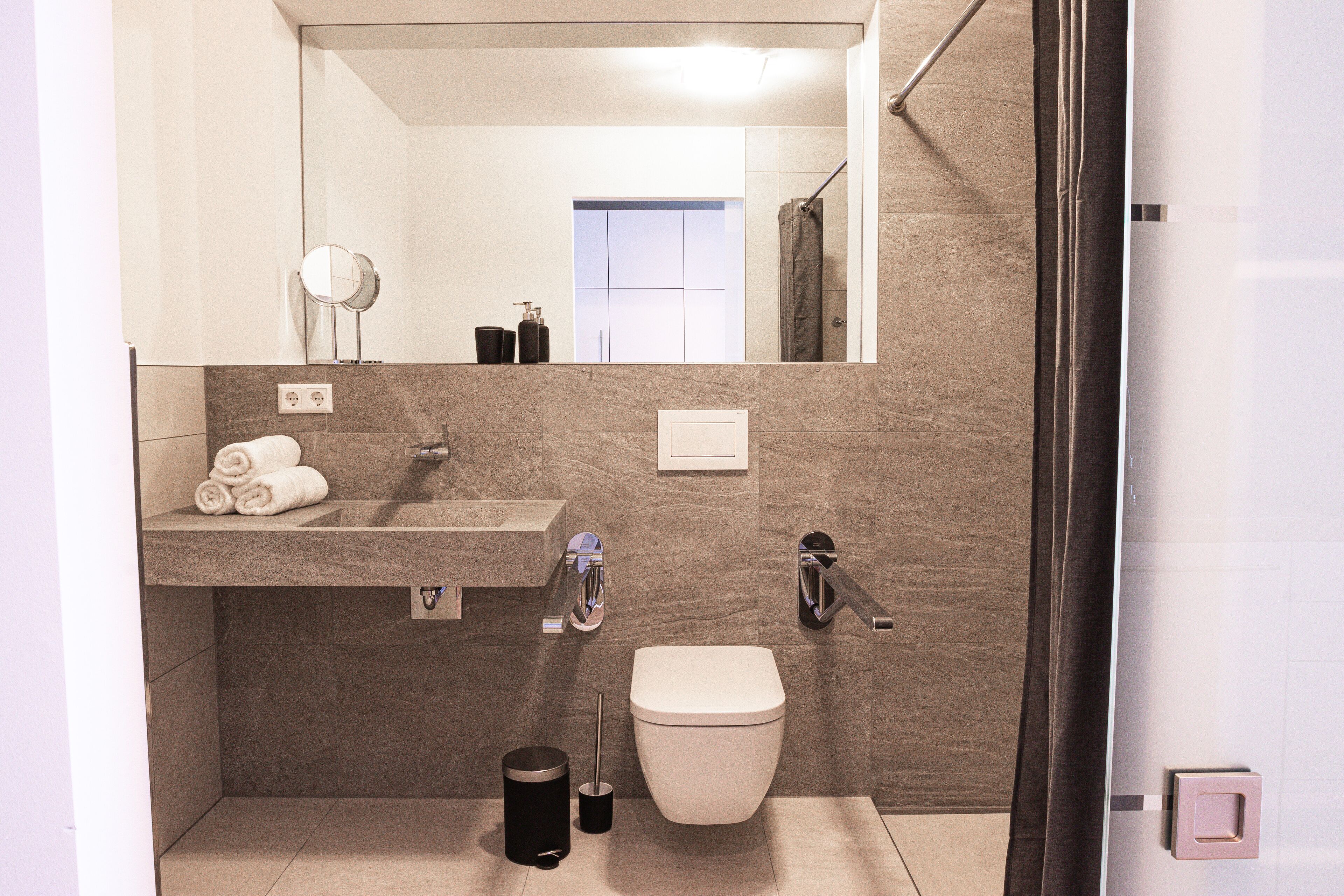 A modern bathroom with a sink, mirror, toilet, and shower.