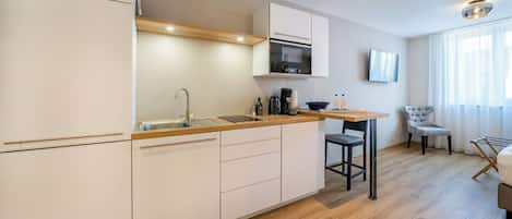 Una cocina moderna con armarios blancos, encimera de madera y horno integrado. Hay una zona de comedor con mesa y sillas.