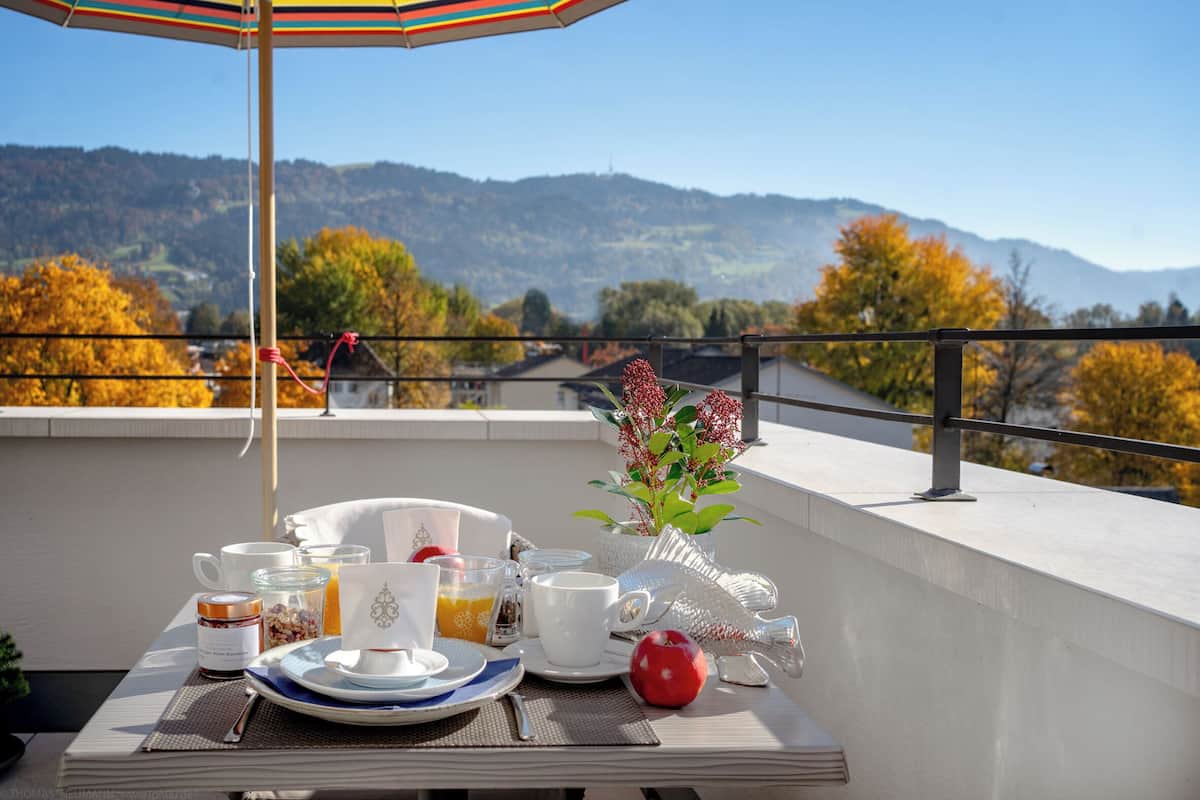 A breakfast setup on a balcony with a table, cups, plates, and a vase of flowers.