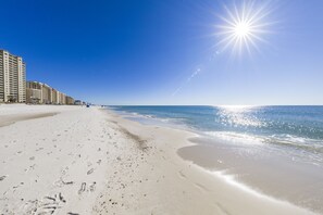 A beach with footprints leading to the water, a clear sky, and buildings in the background.