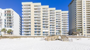 Un hotel sulla spiaggia con diversi balconi, una spiaggia sabbiosa e una scalinata di legno che conduce alla spiaggia.