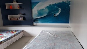 Una camera da letto con un grande affresco raffigurante un surfista su un'onda, scaffali a parete con diversi oggetti e un letto con copripiumino colorato.