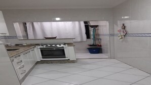 Cucina con mobili bianchi, un fornello e una finestra con tenda.