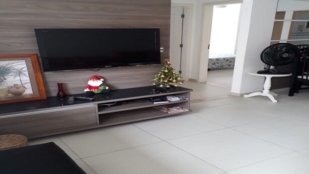 Un soggiorno moderno con una televisione a schermo piatto montata su una parete in legno, un piccolo albero di Natale e una sedia bianca.