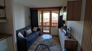A compact living space with a sofa, a small round table, a chair, and a kitchenette area.