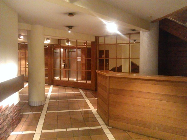 A corridor with tiled flooring, wooden paneling, and a reception desk. - Renovated, fully equipped apartment right at the foot of the slopes! (La Plagne-Tarentaise)