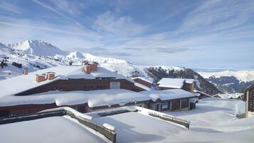A snow-covered mountain village with traditional chalet-style buildings, a ski lift, and a clear view of the surrounding mountains.