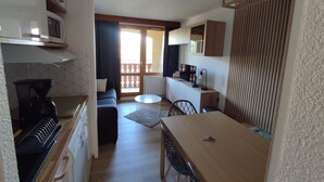A compact kitchen with a microwave, coffee maker, and wooden cabinets. A dining area with a table and chairs is visible, leading to a balcony with a view.
