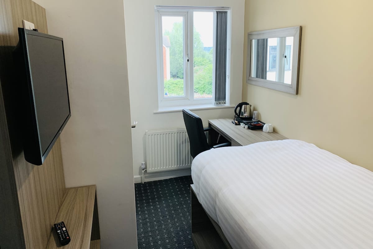 Habitación de hotel con cama, escritorio con silla, televisión, ventana con cortinas y radiador.