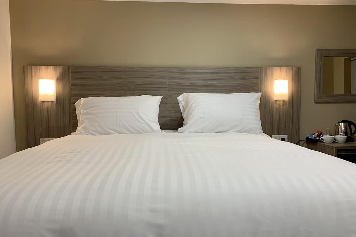 Una cama bien hecha con dos almohadas, cabecera de madera y lámparas de noche.