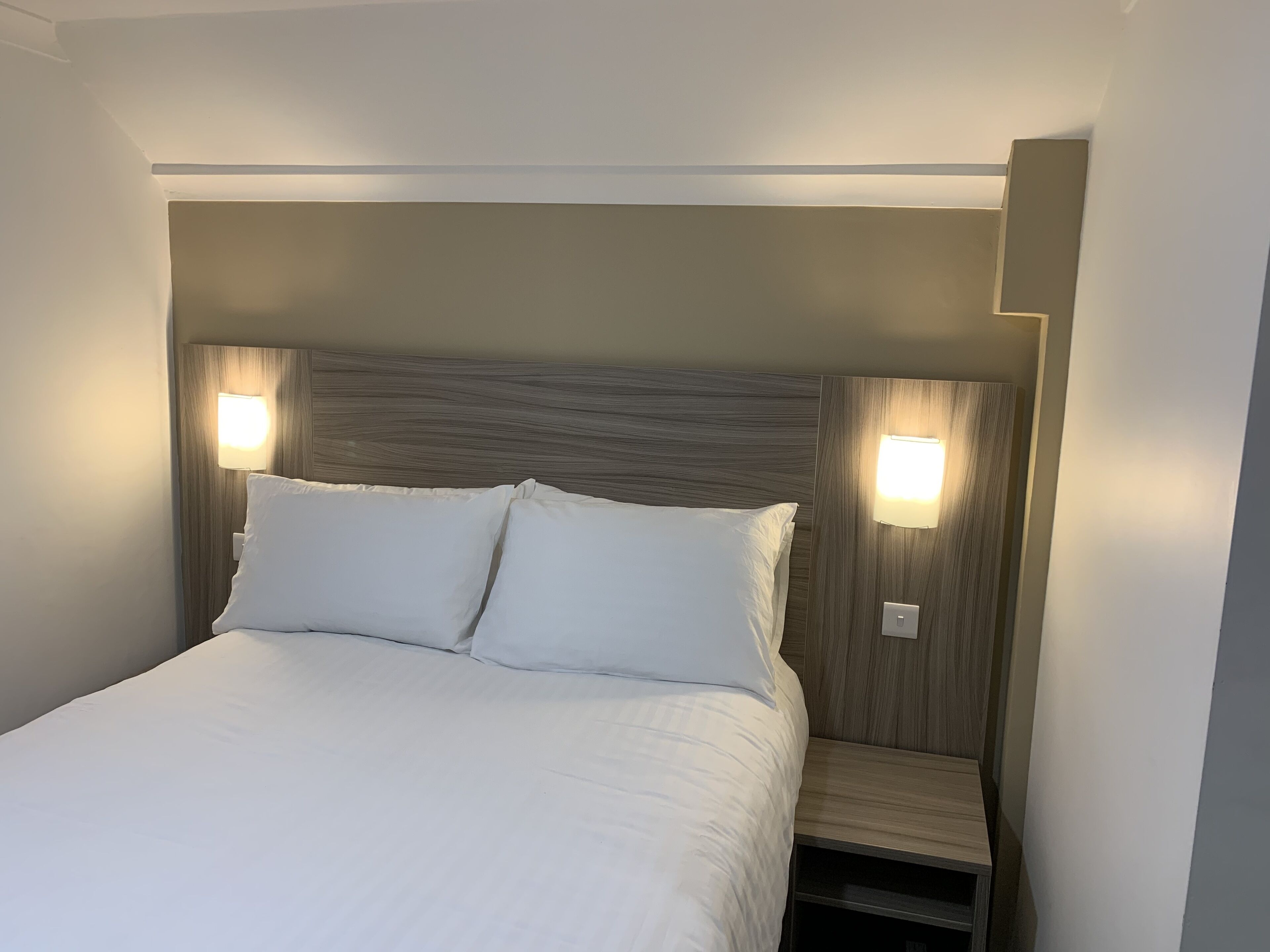 Un lit bien fait, avec deux oreillers et deux lampes de chevet fixées au mur.