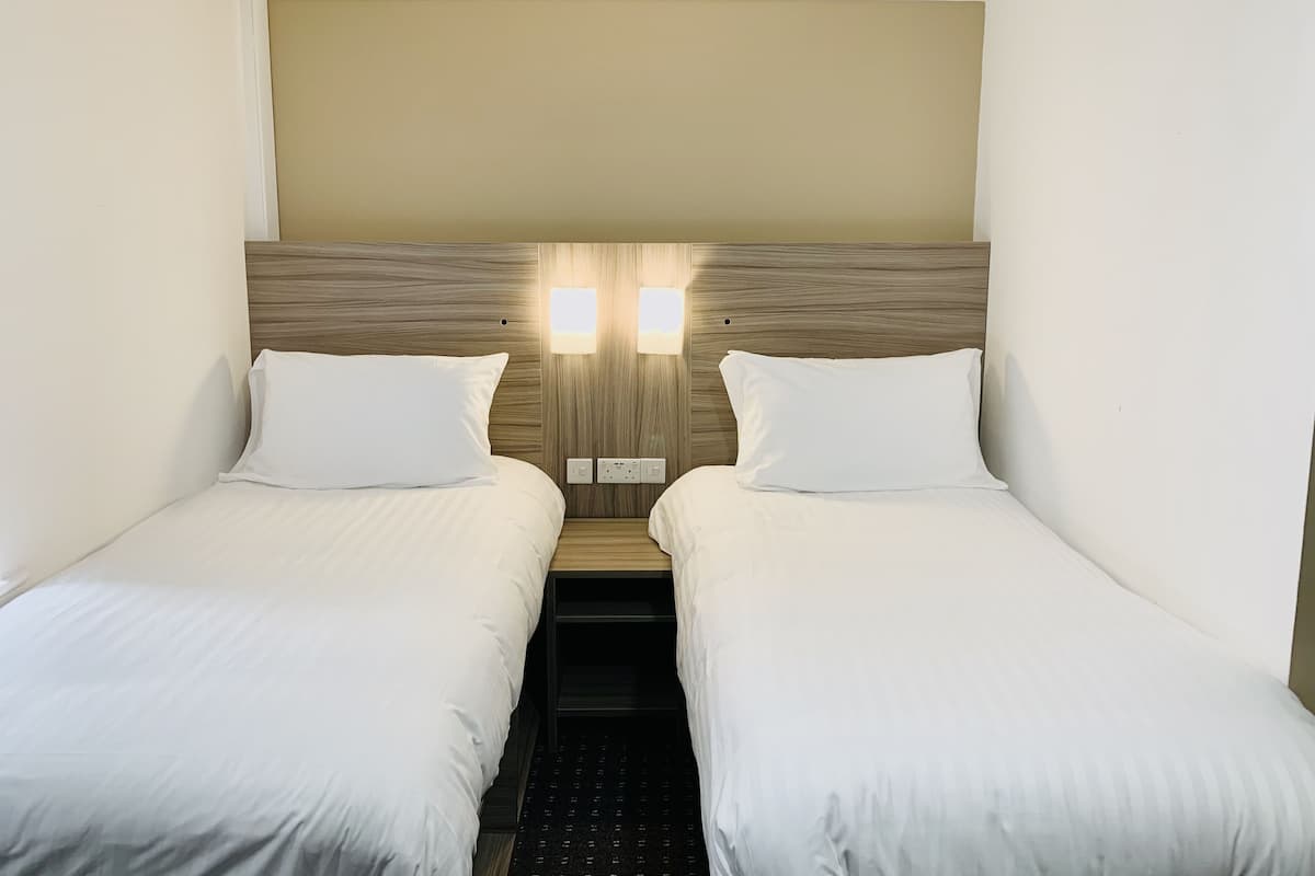 Habitación de hotel con dos camas individuales, cabecero de madera y dos lámparas de pared.