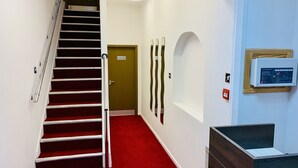 A hotel corridor with a red carpet, a staircase, a 'Staff Only' door, and a control panel on the wall. - De Regency Style Hotel (Redditch)