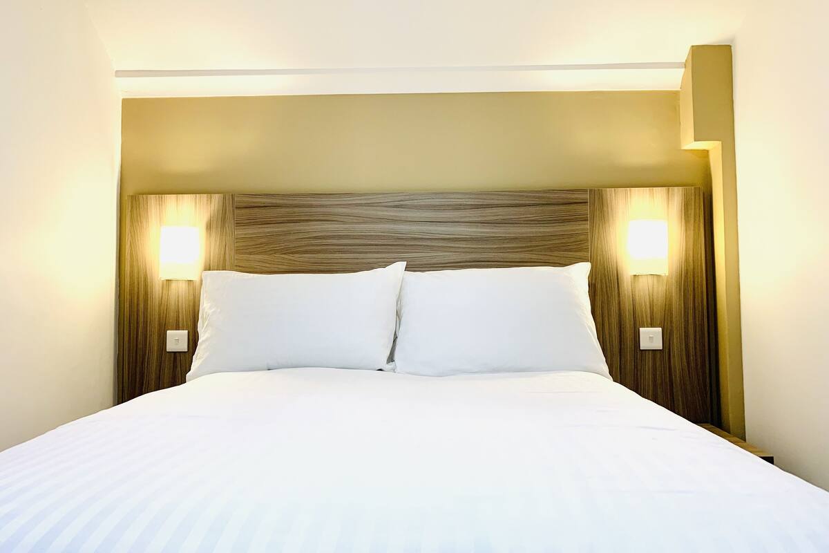 Habitación de hotel con una cama grande, dos lámparas de noche y un cabecero de madera.