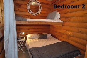 Cozy cabin-style bedroom with a bunk bed, single bed, and bedside table.