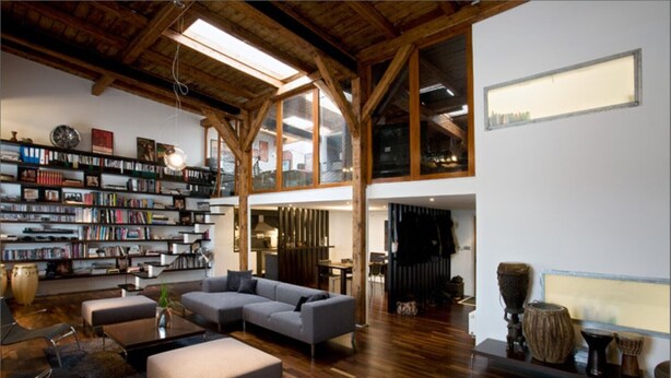 Ein geräumiges Wohnzimmer mit einer großen Eckcouch, einem Couchtisch und einer Bücherwand voller Bücher. Der Raum hat Holzböden und eine hohe Decke mit freiliegenden Balken.