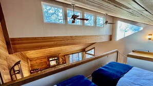 A room with two beds, a wooden ceiling, and a small kitchen area with a stove. - Bright + Beautiful, steps to Old Mammoth + Shuttle (Mammoth Lakes)