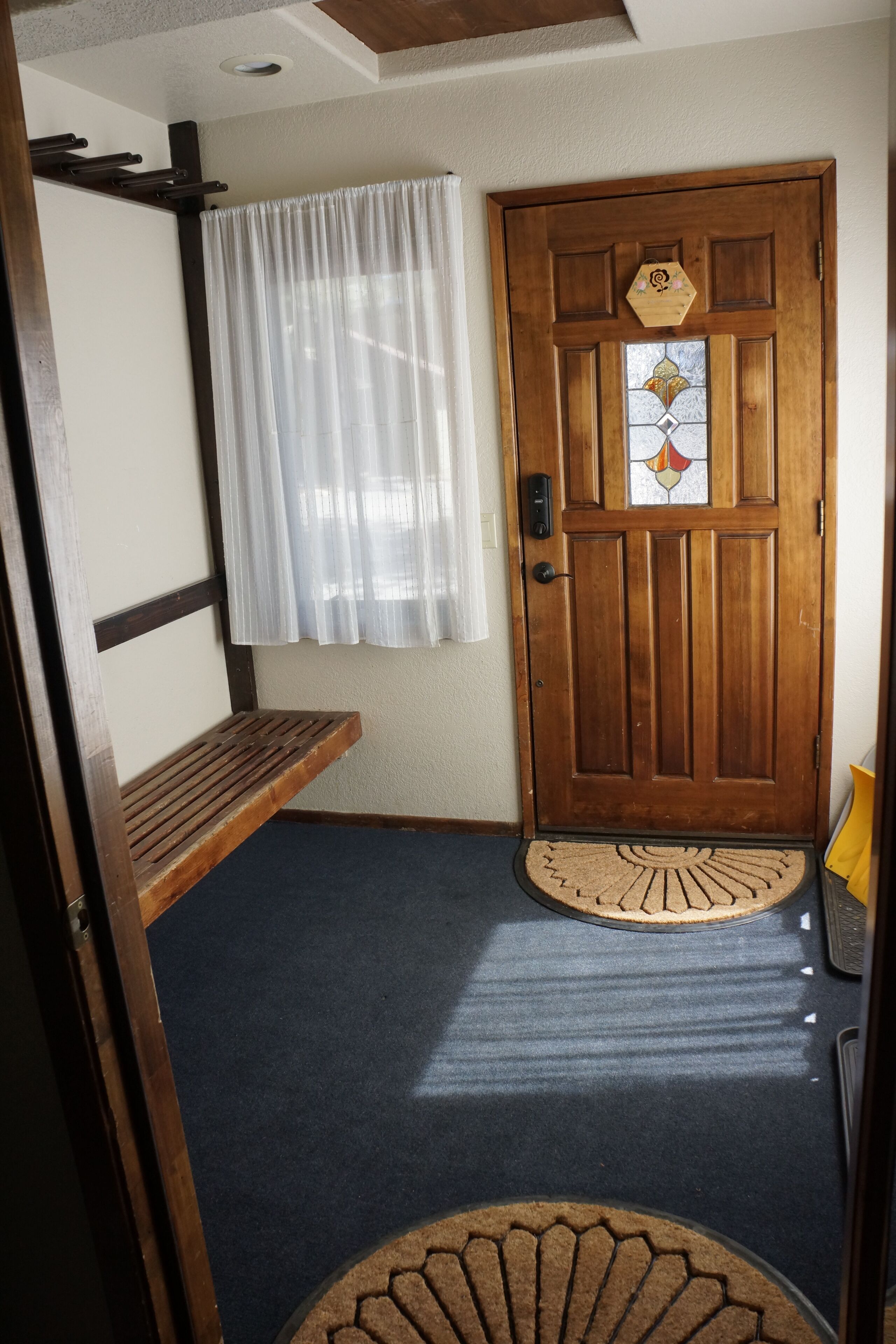 A wooden door with a stained glass window, a bench, and a mat at the entrance.