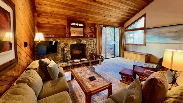 A cozy log cabin interior with a stone fireplace, wooden ceiling, and a comfortable seating area. - Bright + Beautiful, steps to Old Mammoth + Shuttle (Mammoth Lakes)