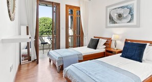 Habitación de hotel con dos camas, un balcón con mesa y sillas, y un cuadro de flores en la pared.