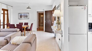 A modern living room with a sofa, dining table, and chairs, a kitchen with a refrigerator, and a wooden door labeled "DD12". - Apartment DD12 - Chloe (Kouklia)