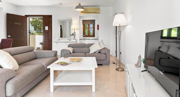 Una sala moderna con un sofá, una mesa de centro blanca, un televisor y una lámpara.