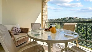 A balcony with wicker furniture, a glass table, and a view of a hilly landscape. - Apartment U3 - Avdimou (Kouklia)