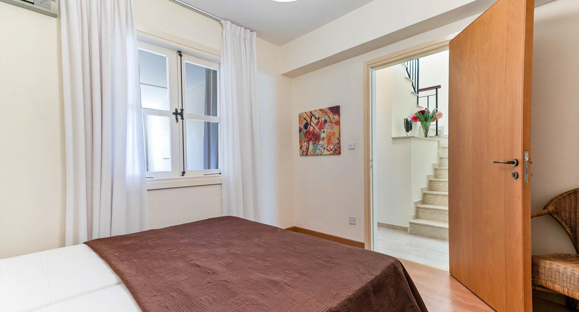 Una camera da letto con un letto, una finestra con tende, un quadro appeso al muro e una scala che conduce a un'altra stanza.