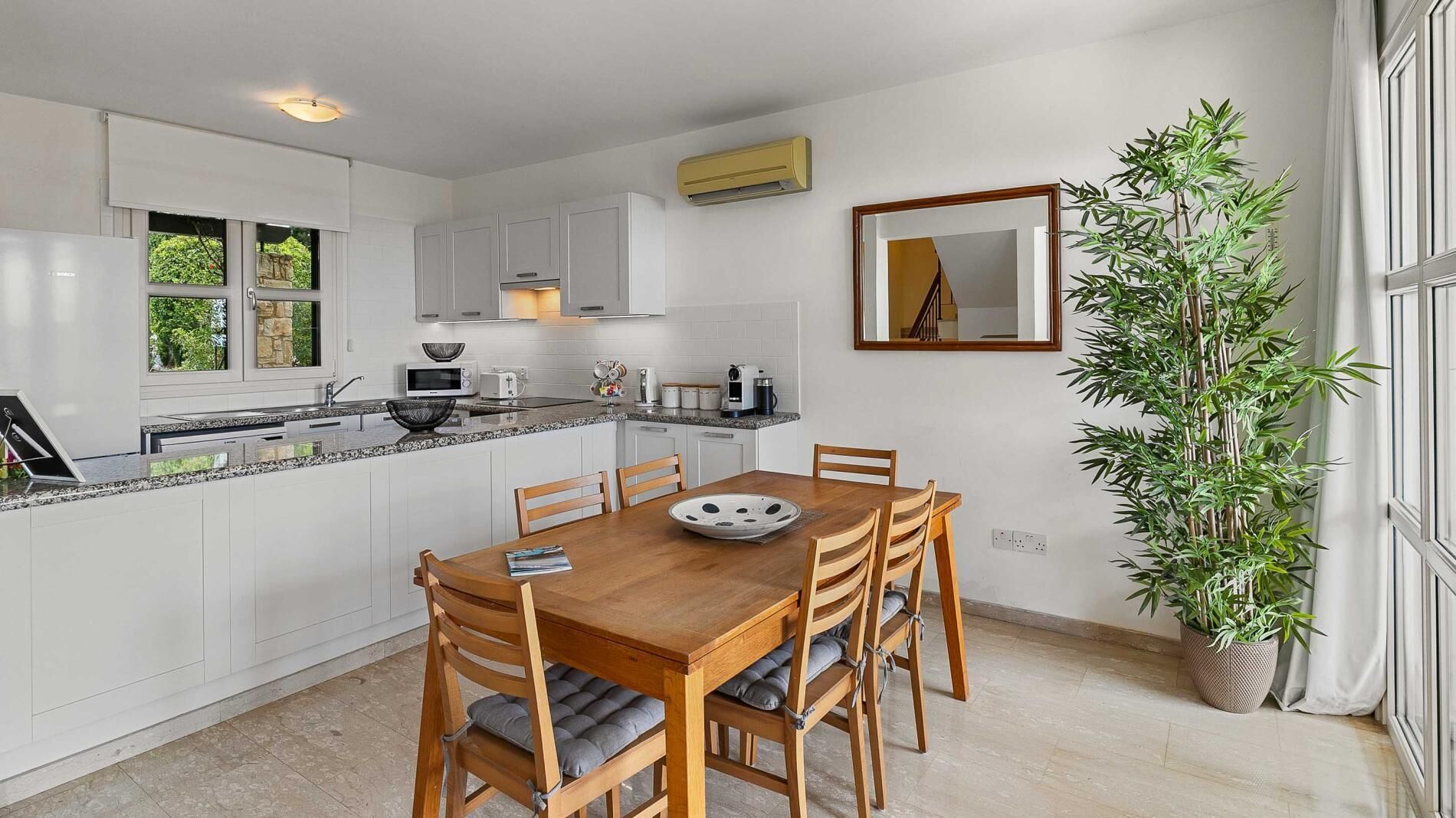 Une cuisine moderne avec des meubles blancs, un plan de travail en granit et un coin repas doté de meubles en bois.