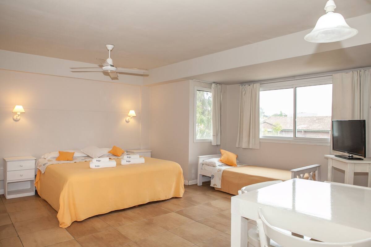A hotel room with two beds, a TV, a ceiling fan, and a window with curtains.