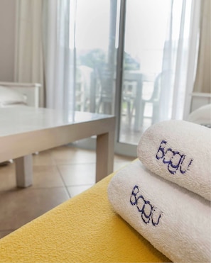 A hotel room with a large window, a yellow towel, and two white towels with "Bagou" embroidered on them. - Bagu Ayres de Mar - Pinamar (Pinamar)
