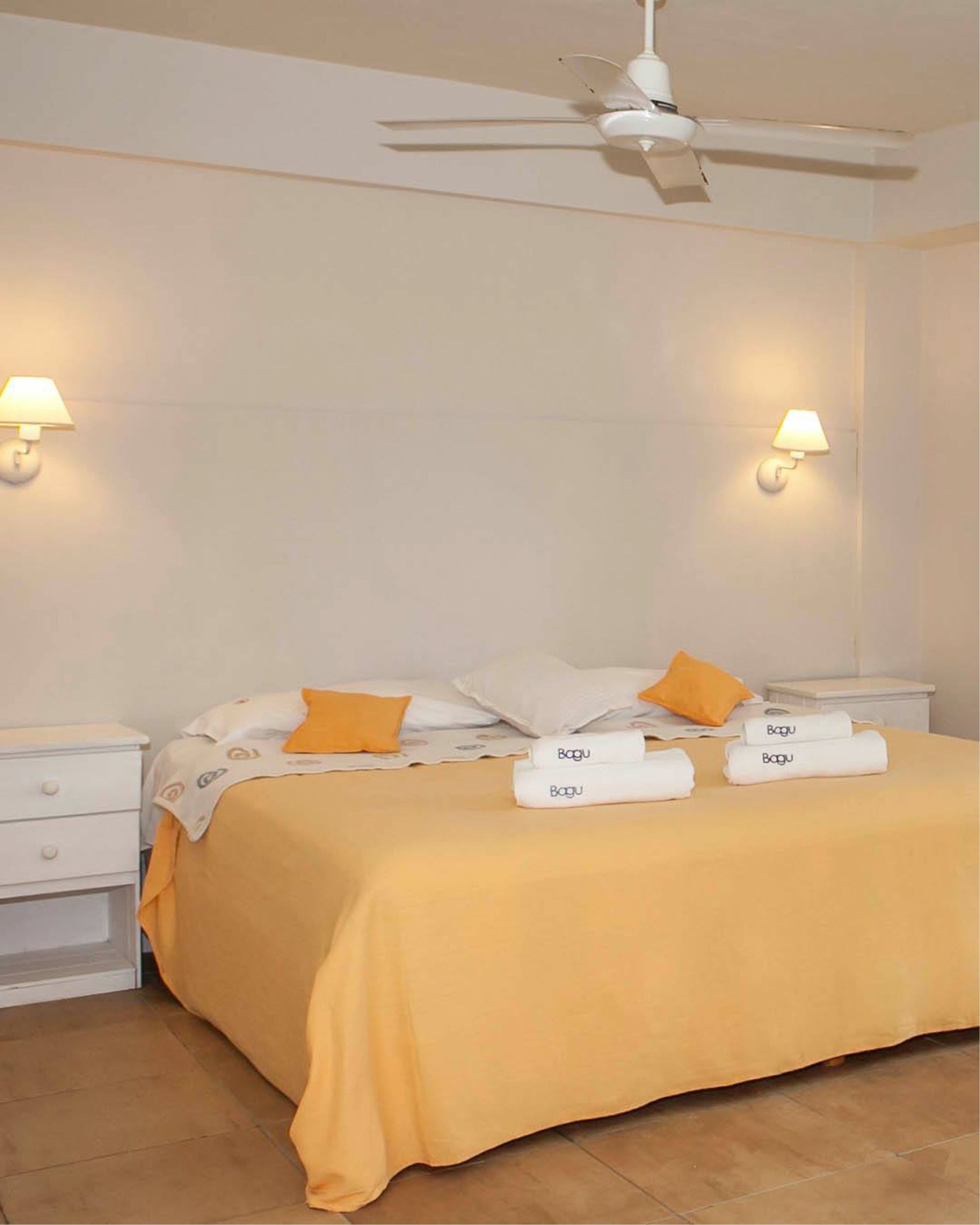 Een hotelkamer met een bed, twee nachtkastjes, een plafondventilator en wandlampen.