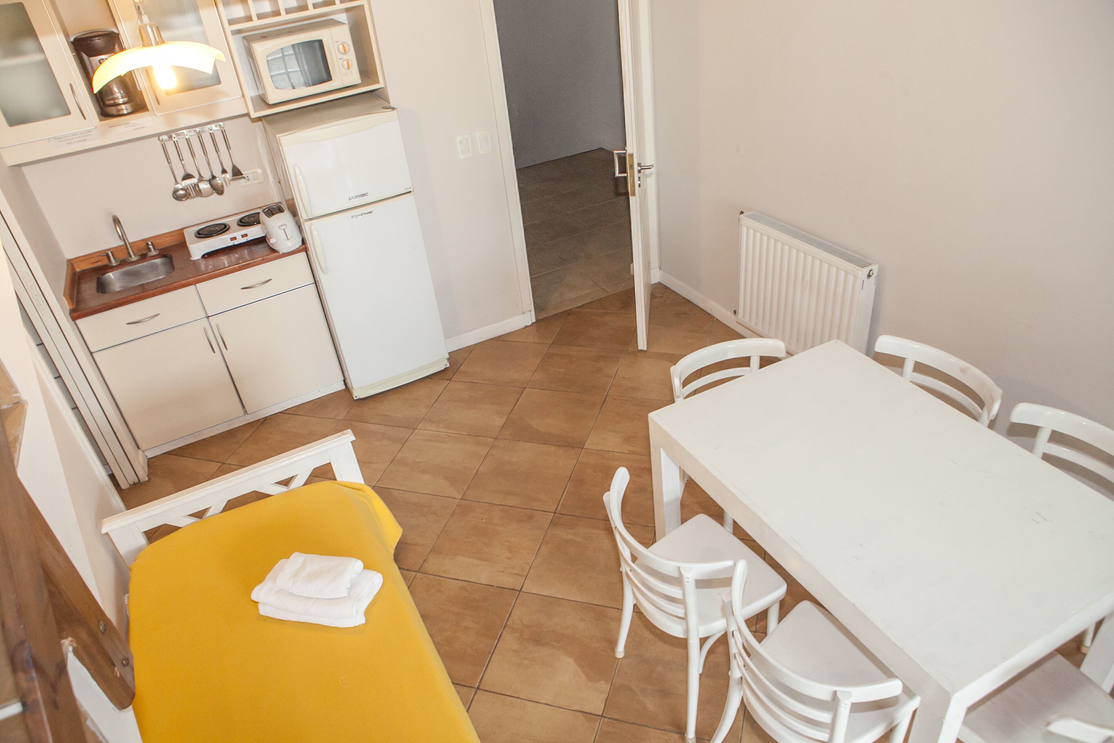 Eine kompakte Küche mit Mikrowelle, Spüle und kleinem Kühlschrank. Es gibt einen Essbereich mit einem weißen Tisch und Stühlen.