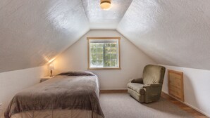 A small attic bedroom with a single bed, a chair, a window, and a ceiling light. - Quiet & comfortable guest house on 20 acre ranch (careywood)