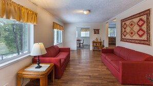 A living room with two red sofas, a wooden coffee table, a lamp, and a large tapestry on the wall. - Quiet & comfortable guest house on 20 acre ranch (careywood)
