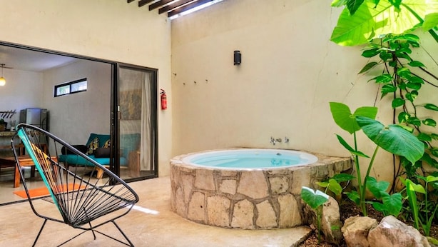 A stone hot tub, a black chair, and a view of a room with a sofa and a window.
