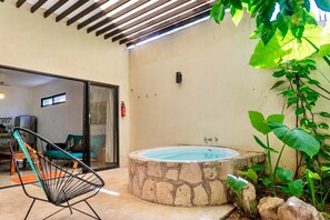 A stone hot tub, a black chair, and a view of a room with a sofa and a window. - Secluded apartment with the best location in Tulum Town (Centro)