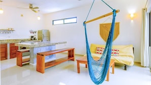 A modern living room with a hammock, wooden furniture, a kitchen area, and a window.