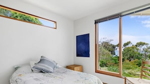Una camera da letto con un letto, un comodino, una sedia, una grande finestra e un'opera d'arte blu appesa al muro.