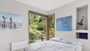 A bedroom with a large bed, a window with a view of greenery, and artwork on the walls.