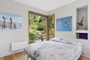 A bedroom with a large bed, a window with a view of greenery, and artwork on the walls.