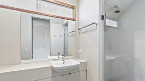 A modern bathroom with a large mirror, two sinks, and a glass shower enclosure.