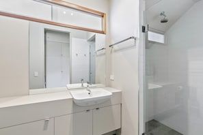 A modern bathroom with a large mirror, two sinks, and a glass shower enclosure.