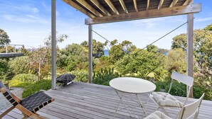 A covered outdoor deck with a table and chairs, overlooking a lush garden and a body of water.