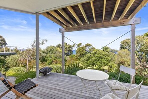 A covered outdoor deck with a table and chairs, overlooking a lush garden and a body of water.