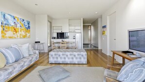 A modern living room with a sofa, ottoman, and a TV on a wooden table.