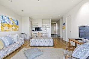 A modern living room with a sofa, ottoman, and a TV on a wooden table.