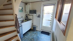 Une cuisine équipée d’un four à micro-ondes, d’un évier et d’une cuisinière, donnant sur une porte qui offre une vue sur l’extérieur.