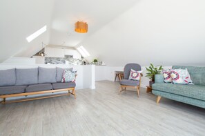 A modern loft apartment with a living area featuring a grey sofa, a teal sofa, and a wooden dining table.