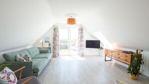 Un salon spacieux avec un canapé vert, un meuble en bois et un téléviseur fixé au mur.